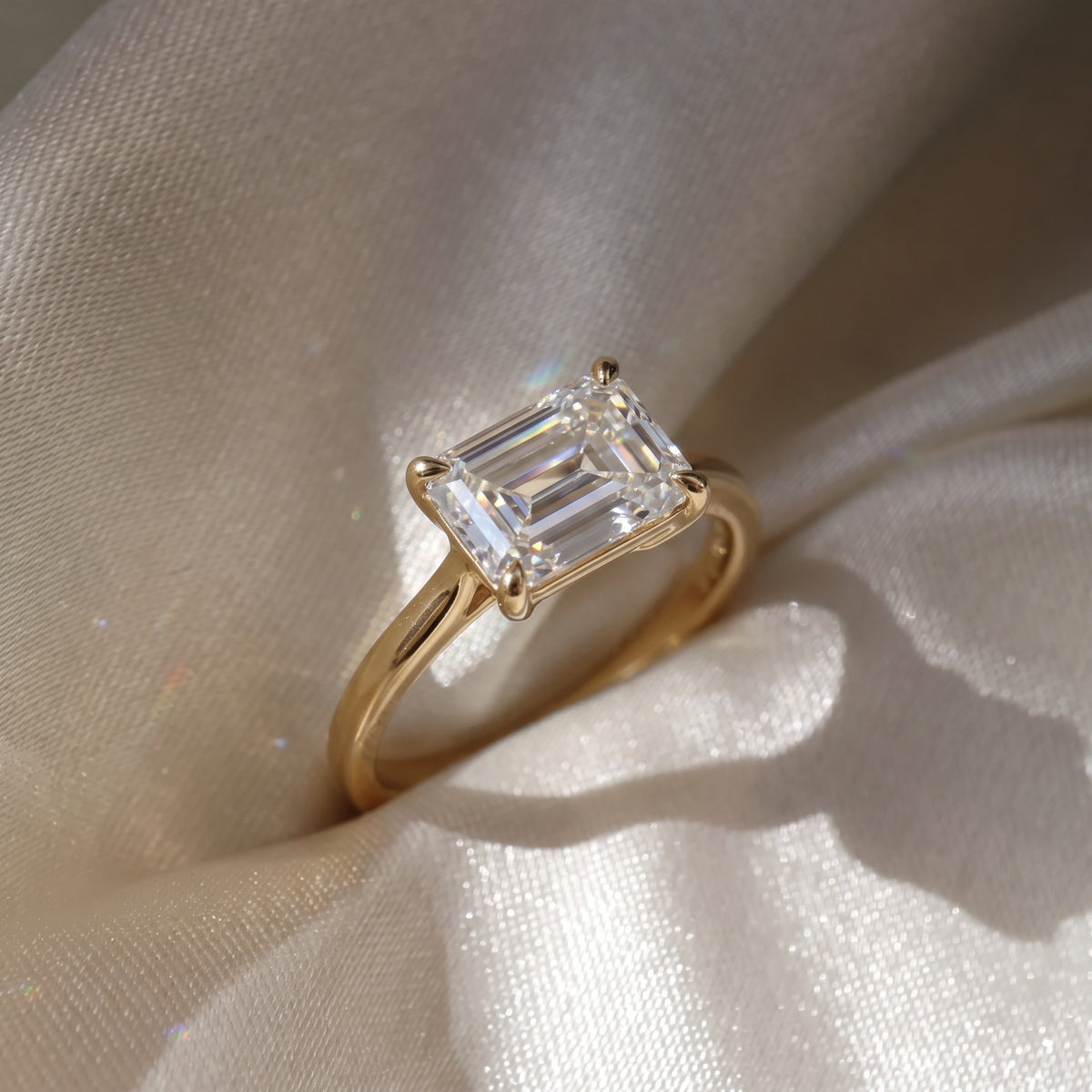The Aria Ring — East-West Emerald Solitaire Lab-Grown Diamond Engagement Ring in Yellow Gold on a Silk Cream Fabric | The Jewel Concierge