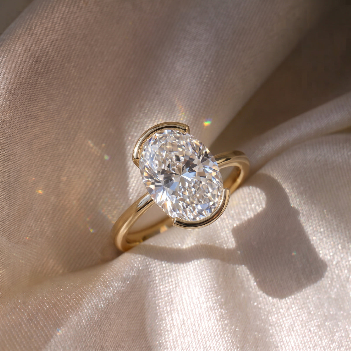 The Celine Ring — Oval Half Bezel Solitaire Lab-Grown Diamond Engagement Ring in Yellow Gold on Silk Fabric | The Jewel Concierge