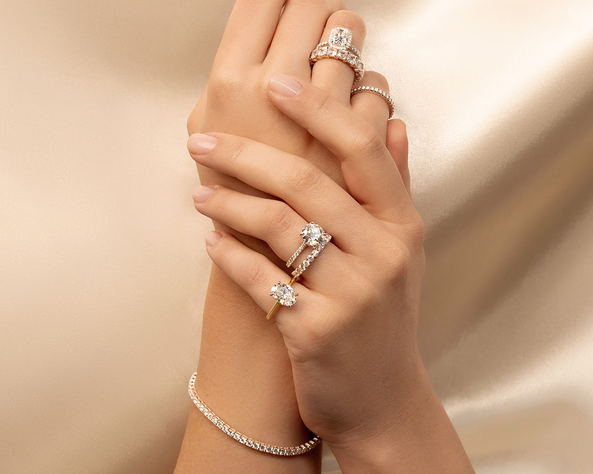 woman's hands with mutliple diamond jewellery rings and tennis bracelet on a soft luxurious background