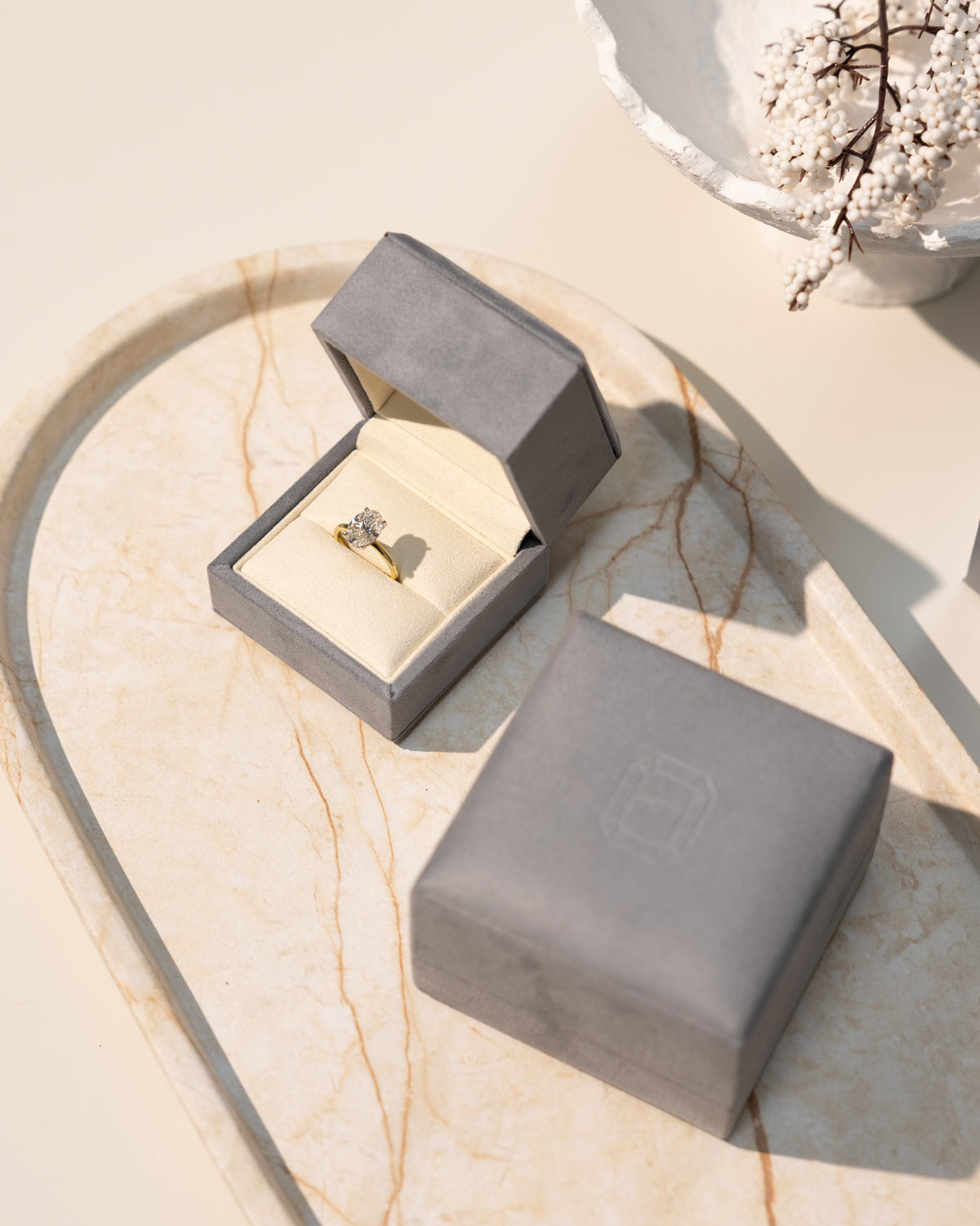 stylish & luxurious gry ring box with an oval diamond engagement ring on a marble tray