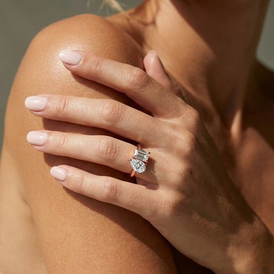 A close-up lifestyle shot of a woman's hand resting on her shoulder, wearing The Eloise Toi Et Moi Engagement Ring in 18K rose gold, featuring a pear and emerald cut lab-grown diamonds | The Jewel Concierge