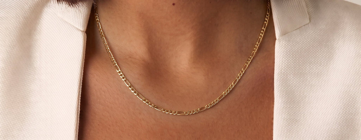 A close-up of a model wearing The Figaro gold Chain, styled with a cream-colored blazer.