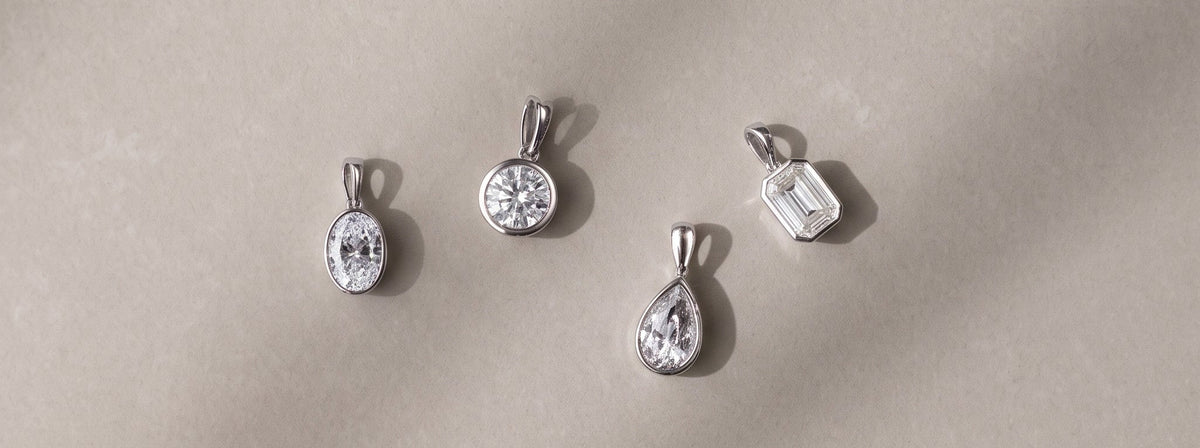 Four Odette Bezel pendants elegantly laid on a luxurious grey background - The Jewel Concierge