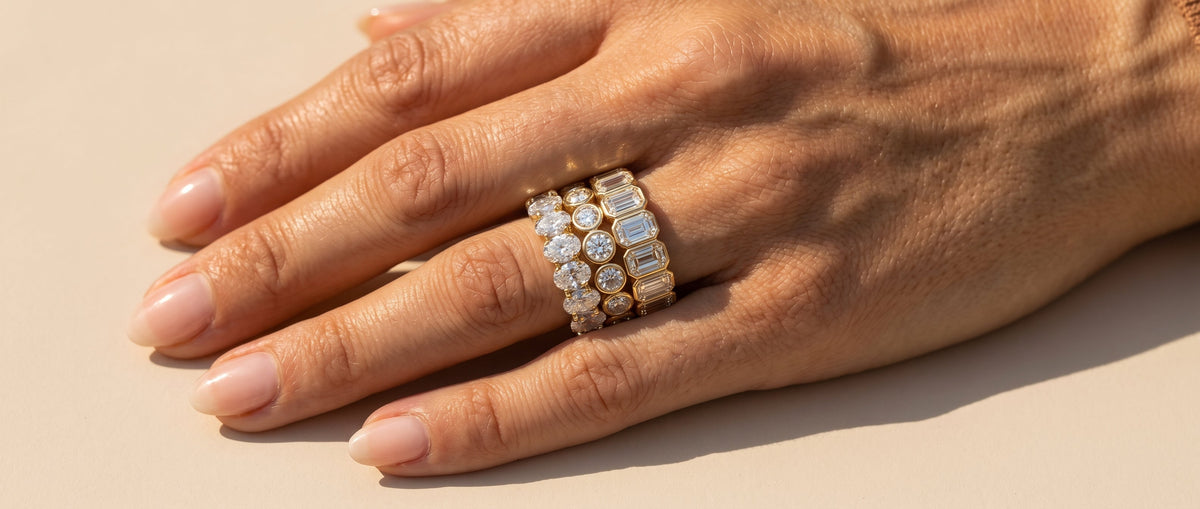 Close up of a model's hand, featuring three eternity rings with lab-grown diamonds in various shapes, set in 18K yellow gold - The Jewel Concierge