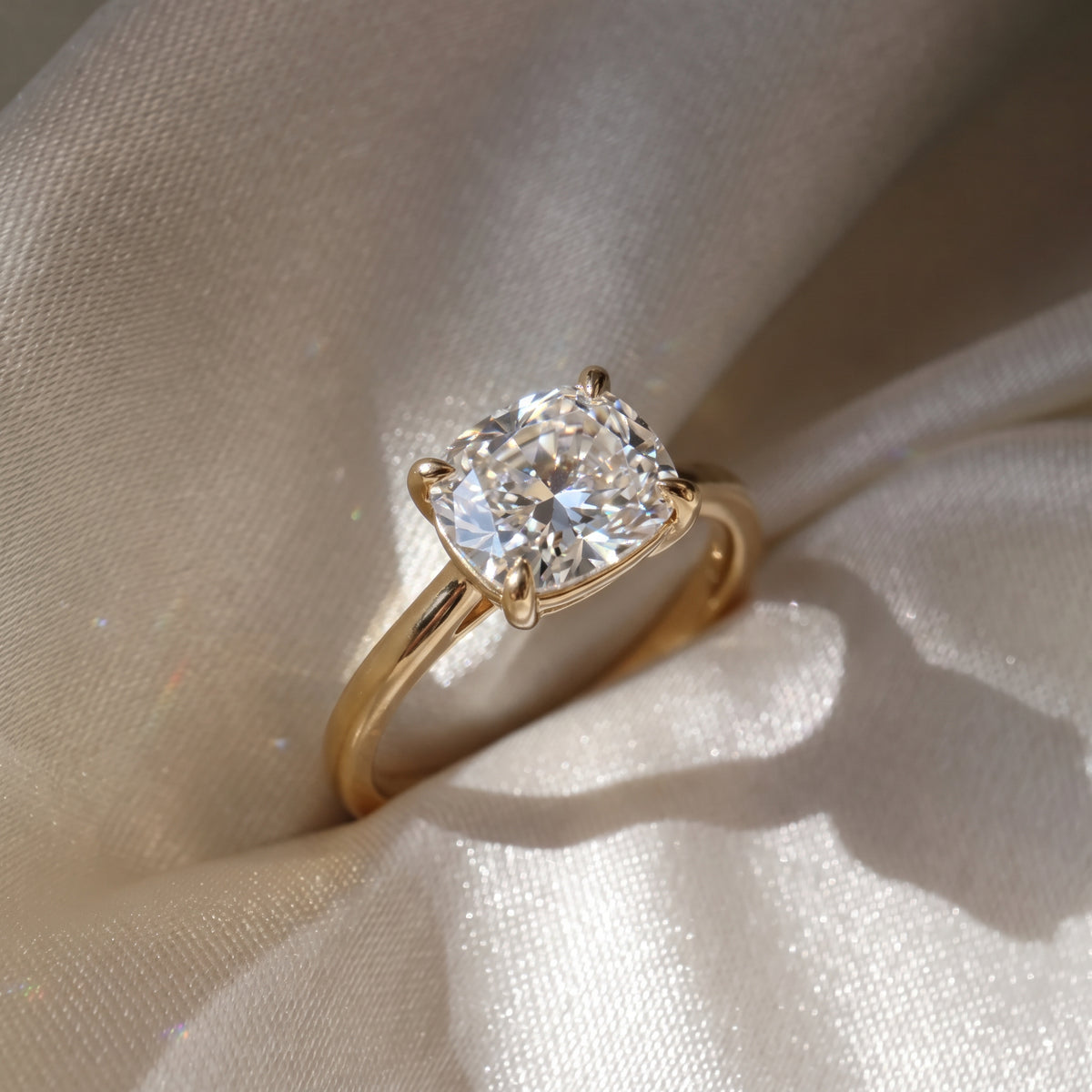 The Aria Ring — East-West Elongated Cushion Solitaire Lab-Grown Diamond Engagement Ring in Yellow Gold on a Silk Cream Fabric  | The Jewel Concierge