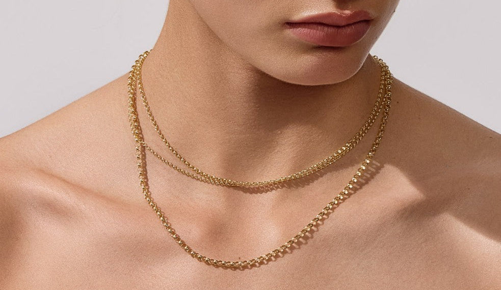Woman wearing a gold necklace and earrings against a neutral background