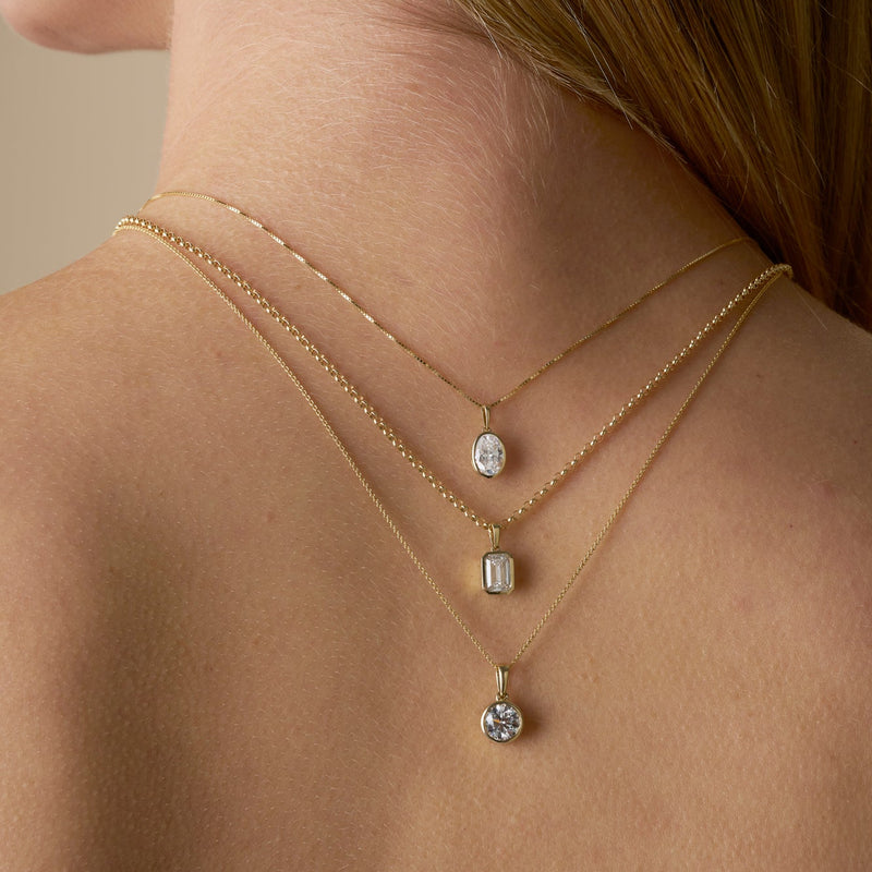A close-up of a woman's back and neck showing multiple gold necklaces with a bezel-set lab-grown diamond - The Jewel Concierge