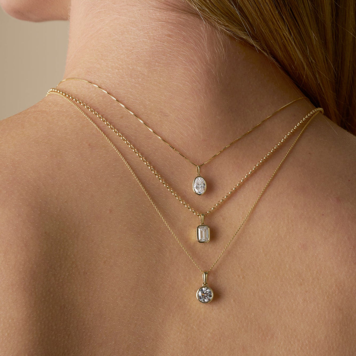 A close-up of a woman's back and neck showing multiple gold necklaces with a bezel-set lab-grown diamond - The Jewel Concierge