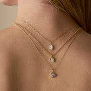 A close-up of a woman's back and neck showing multiple gold necklaces with a bezel-set lab-grown diamond - The Jewel Concierge