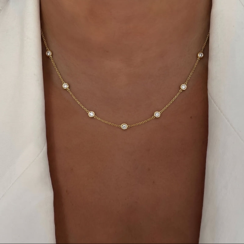 Close up of a model showcasing a Diamond Bezel By The Yard by gold chain necklace featuring nine small, round bezel-set lab-grown diamonds spaced evenly along the chain - The Jewel Concierge