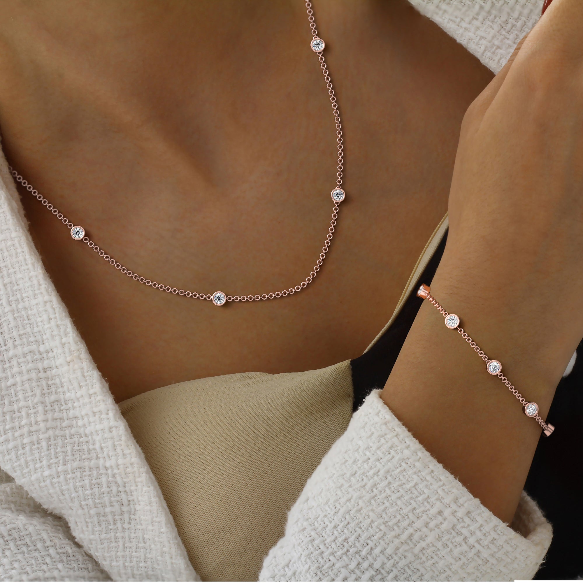 Rose gold bezel by the yard necklace and bracelet with small round diamonds on woman wearing a beige outfit.