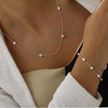 Rose gold bezel by the yard necklace and bracelet with small round diamonds on woman wearing a beige outfit.