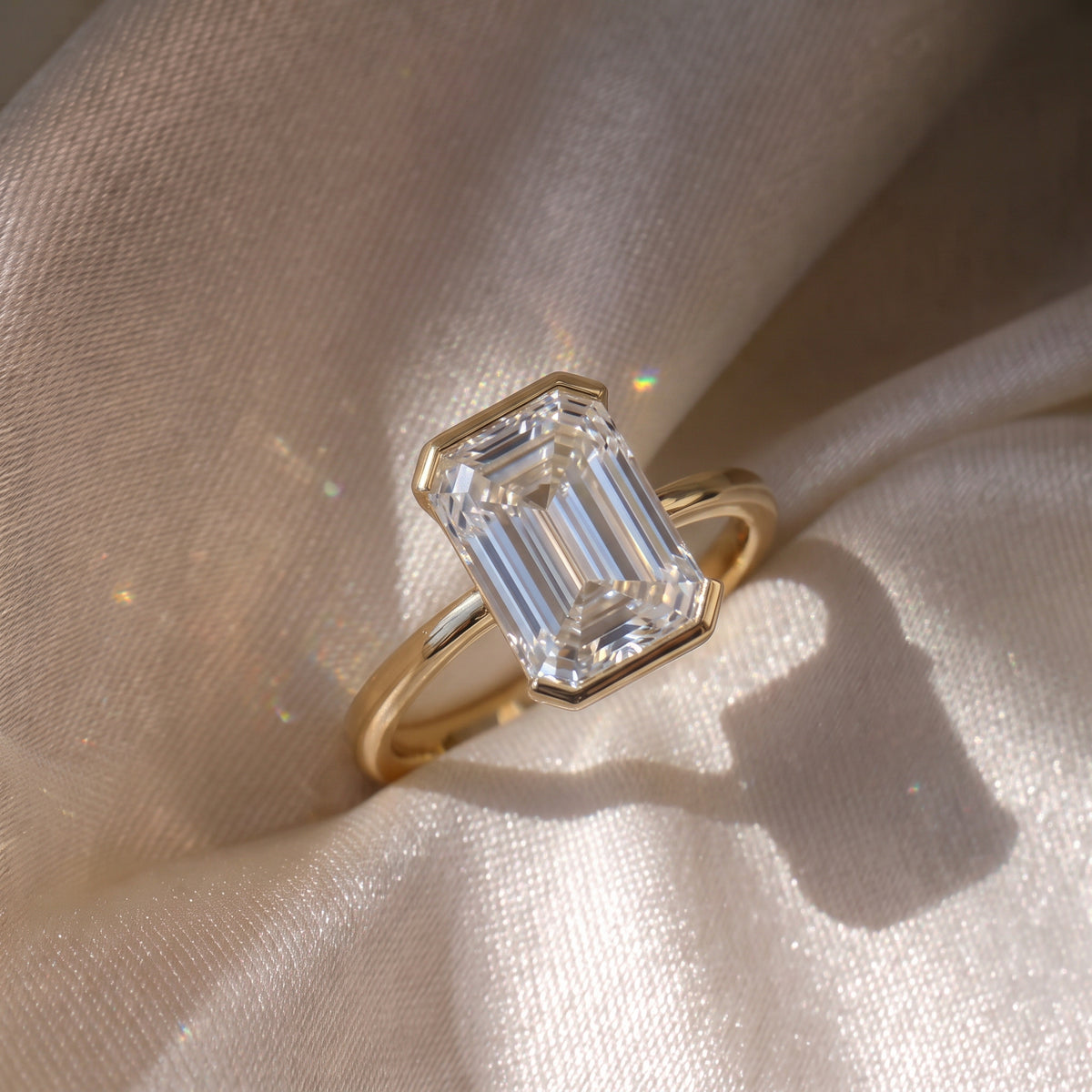 The Celine Ring — Emerald Half Bezel Solitaire Lab-Grown Diamond Engagement Ring in Yellow Gold on a luxurious silk fabric | The Jewel Concierge