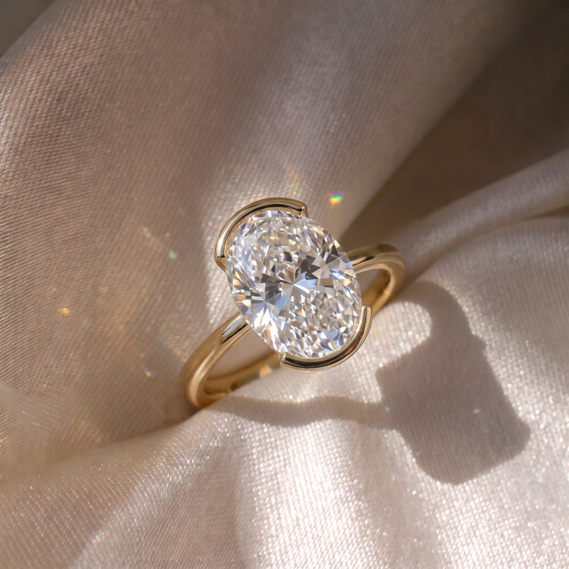 The Celine Ring — Oval Half Bezel Solitaire Lab-Grown Diamond Engagement Ring in Yellow Gold on Silk Fabric | The Jewel Concierge