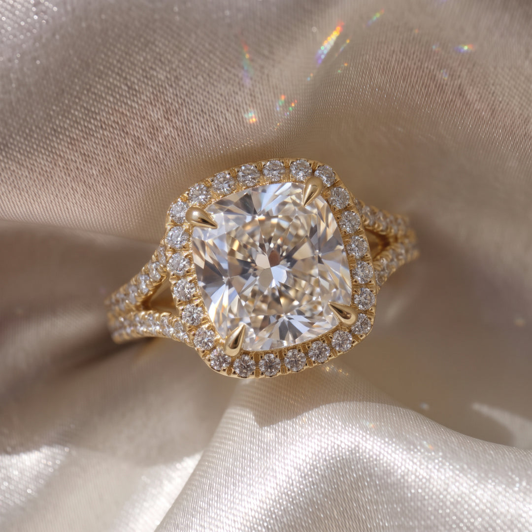 Elara Ring - Cushion Orbital Halo with split pave band in 18K yellow gold on a luxurious silk fabric - The Jewel Concierge