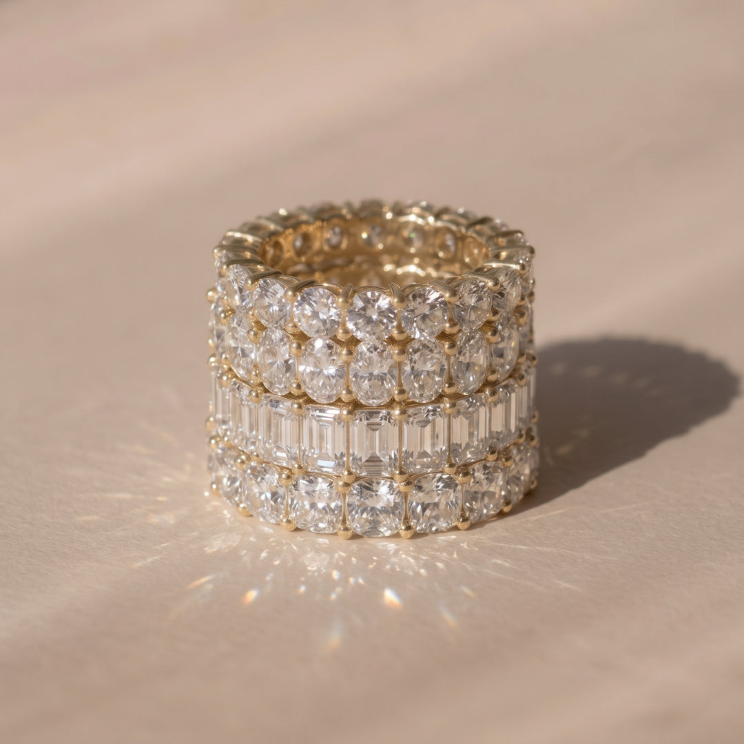 A close-up of four lab-grown diamond eternity rings in different shapes, resting on a warm beige surface with a soft shadow | The Jewel Concierge