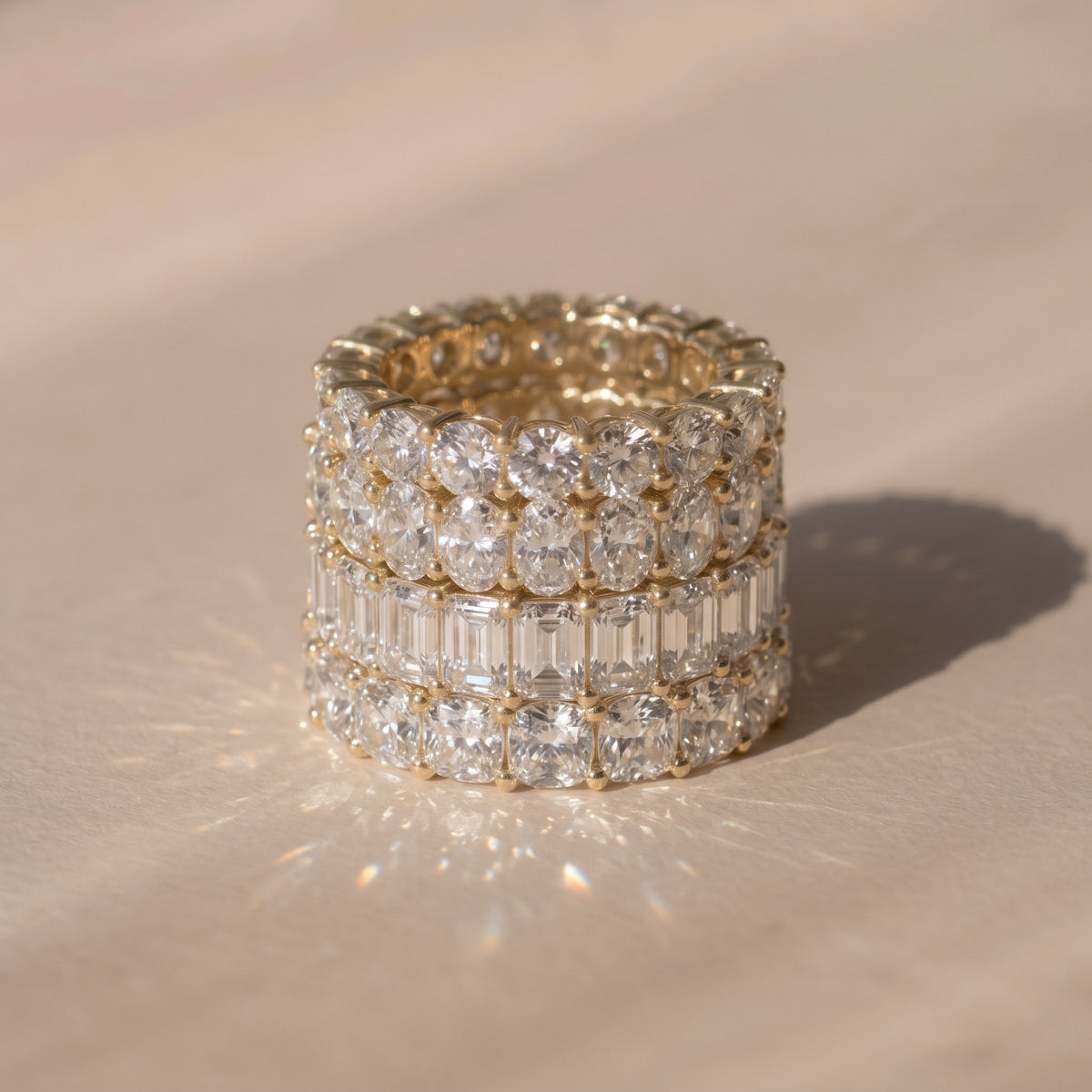 A close-up of four lab-grown diamond eternity rings in different shapes, resting on a warm beige surface with a soft shadow | The Jewel Concierge