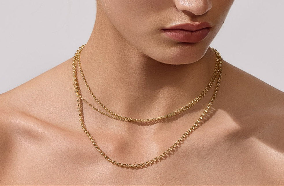 Woman wearing a gold necklace and earrings against a neutral background