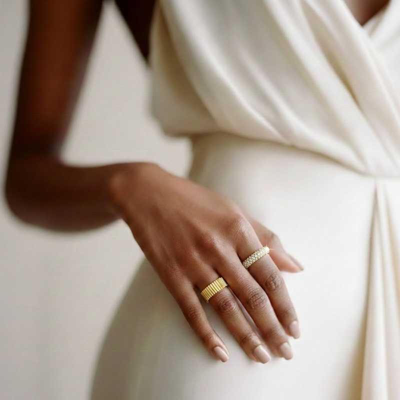 Hand wearing two gold rings on a neutral background