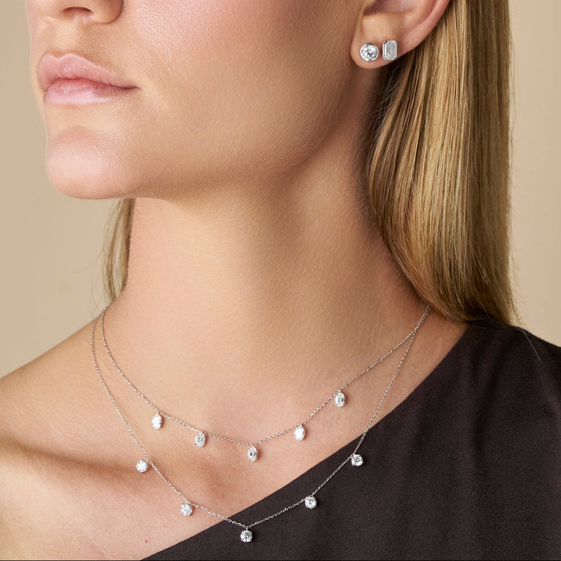 Close up of a model wearing two Necklaces featuring 5 lab-grown diamonds elegantly suspended on a fine gold chain against a solid beige background - The Jewel Concierge