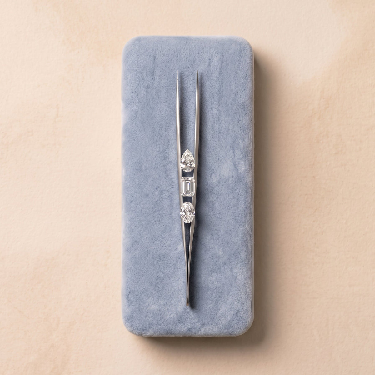 Lab-grown diamonds placed on tweezers, resting on a light blue soft cushion against a warm champagne background | The Jewel Concierge
