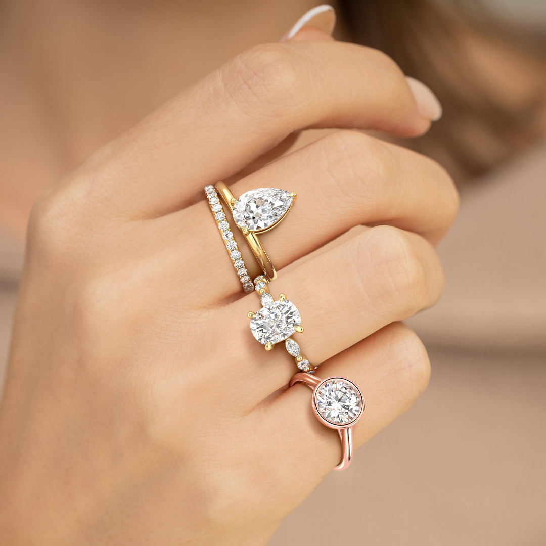 Hand wearing three lab-grown diamond rings on a neutral beige background