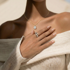 Close-up of a person wearing a pear cut diamond pendant and an open wrap around gold ring, with a neutral background.