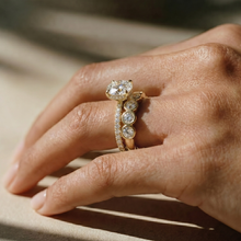 close up of a woman's hand, adorned with a stunning round brilliant lab grown diamond engagement ring with a pave band,  paired with a bezel set oval half eternity ring, both in 18K yellow gold - The Jewel Concierge.