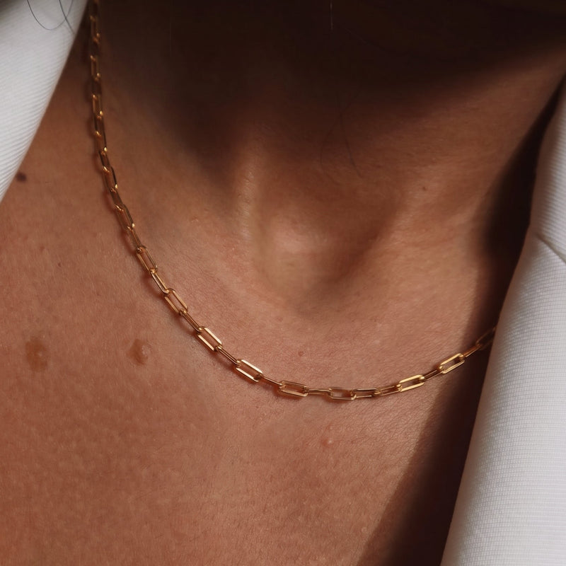 A close-up of a model showcasing a delicate gold paperclip chain necklace, styled with a cream blazer - The Jewel Concierge