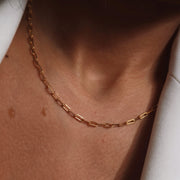 A close-up of a model showcasing a delicate gold paperclip chain necklace, styled with a cream blazer - The Jewel Concierge