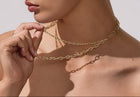 Close-up of a woman wearing gold chain necklaces and earrings against a neutral background