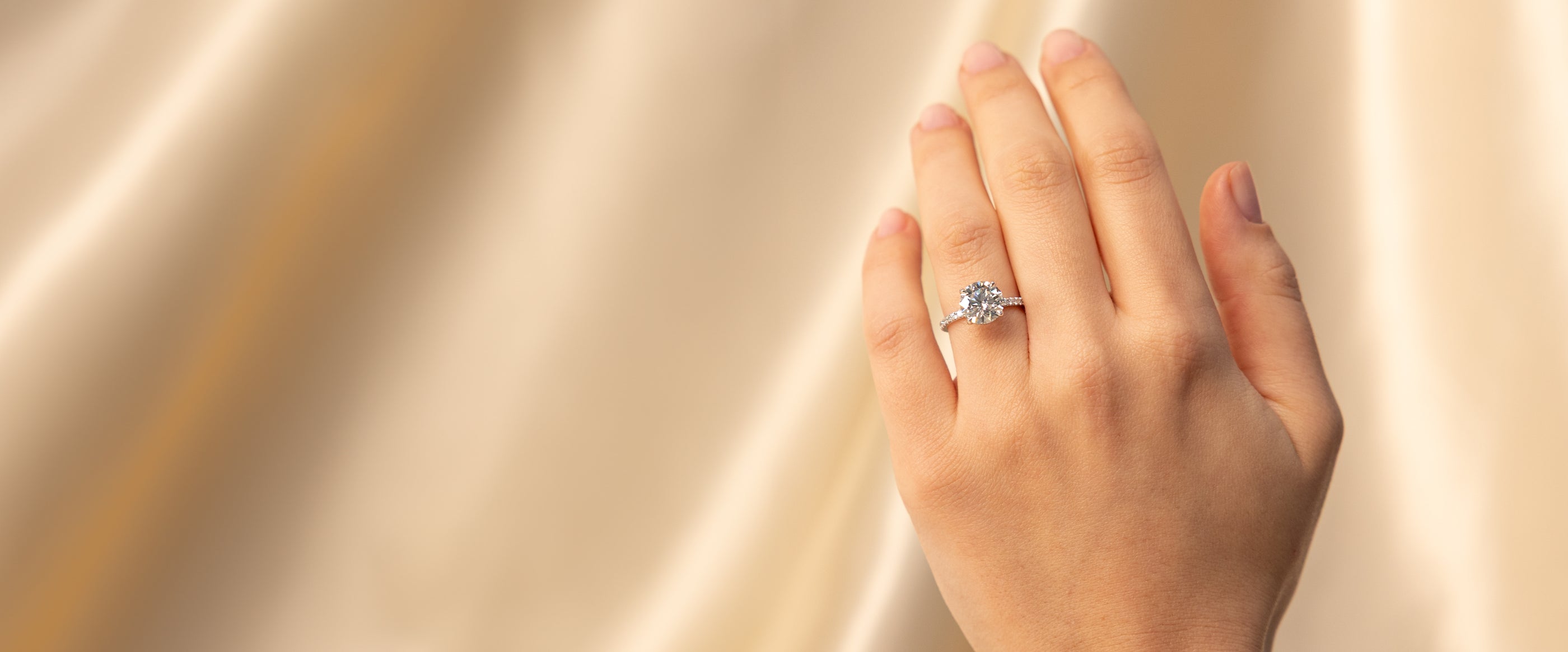 Hand wearing a diamond ring on a soft, neutral background
