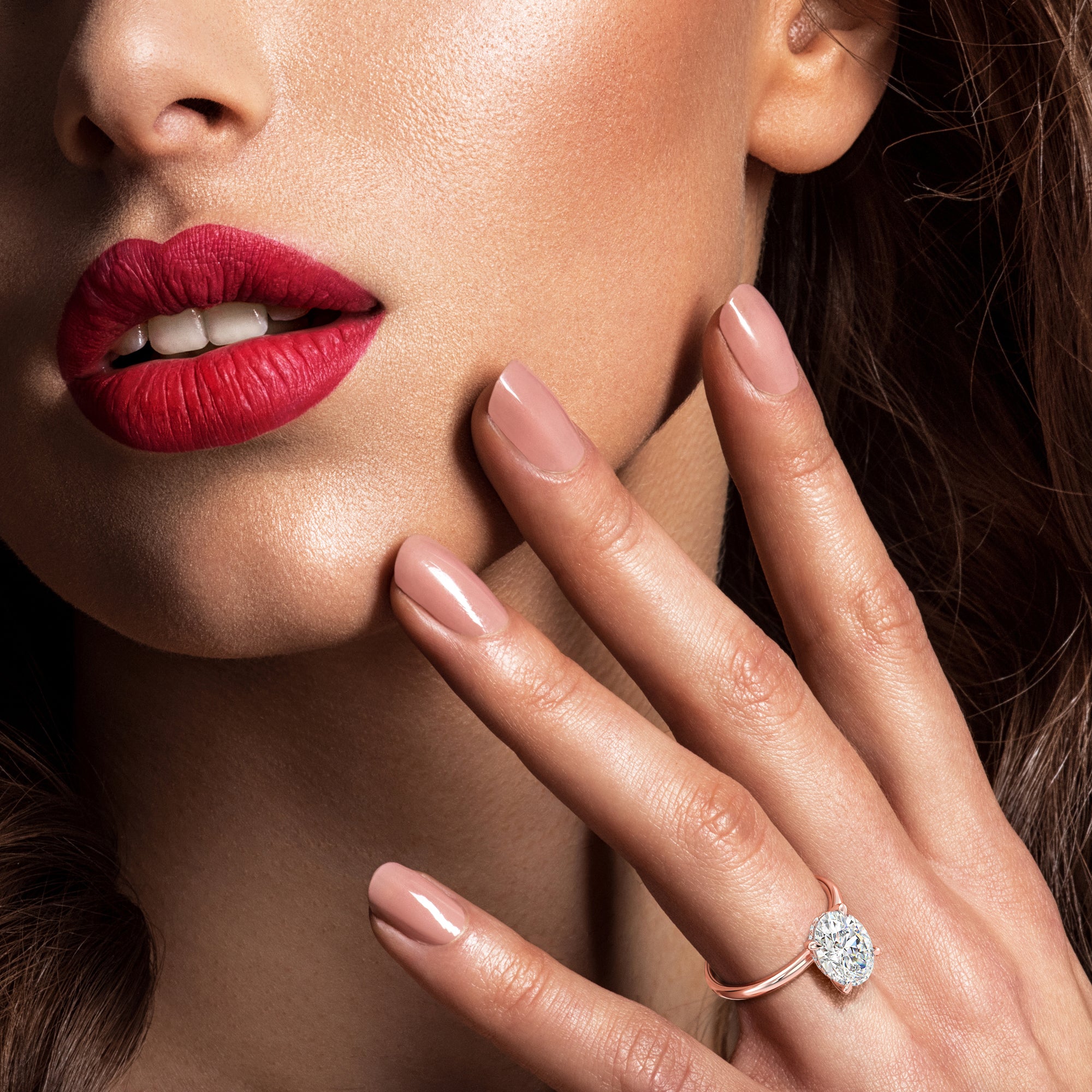 Close-up of a woman's face with red lipstick and a dazzling solitaire diamond ring in rose gold.