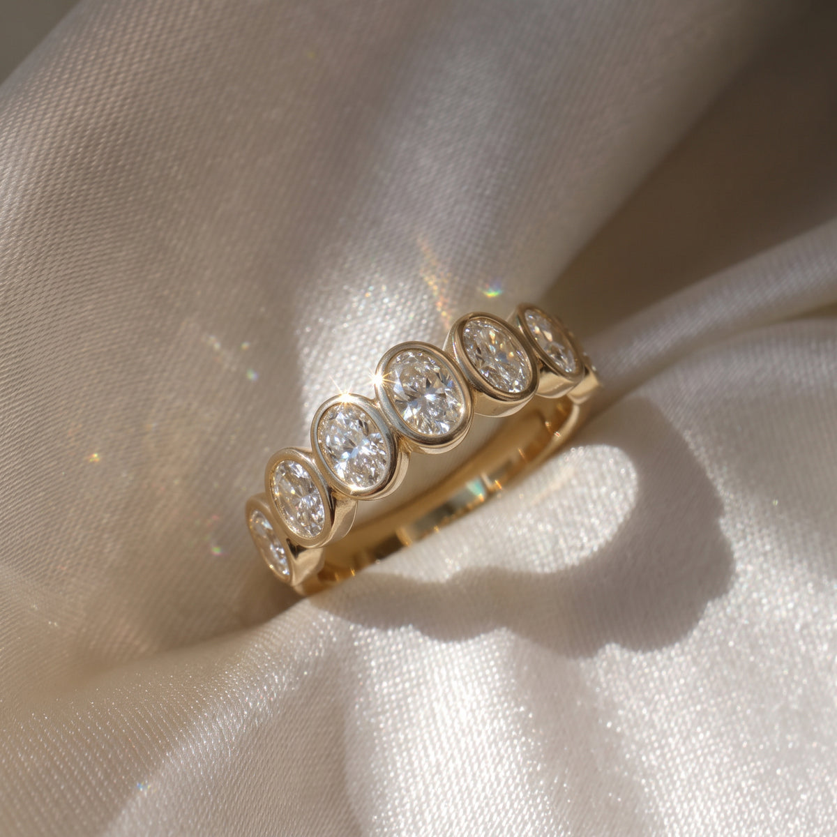 The Sara Ring — Oval Bezel Set Half Lab-Grown Diamond Eternity Band in Yellow Gold on a luxurious silk fabric| The Jewel Concierge