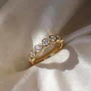The Sara Ring — Round Bezel Set Half Lab-Grown Diamond Eternity Band in Yellow Gold on a luxurious silk fabric| The Jewel Concierge