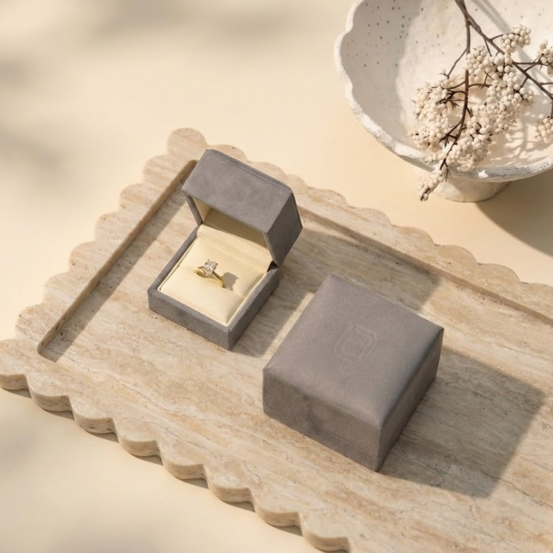 Oval lab-grown diamond engagement ring in 18K yellow gold, elegantly placed inside The Jewel Concierge signature ring box and laid on a travertine tray | The Jewel Concierge