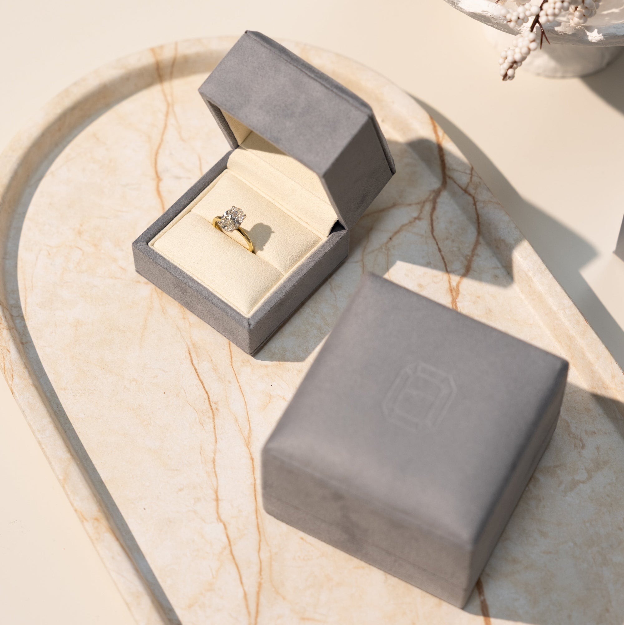stylish & luxurious gry ring box with an oval diamond engagement ring on a marble tray