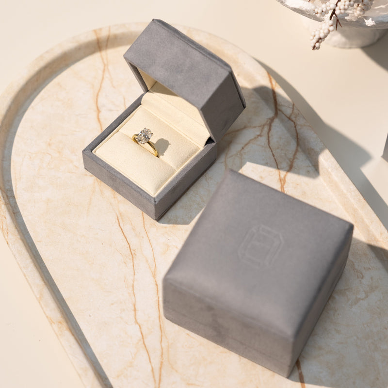stylish & luxurious gry ring box with an oval diamond engagement ring on a marble tray
