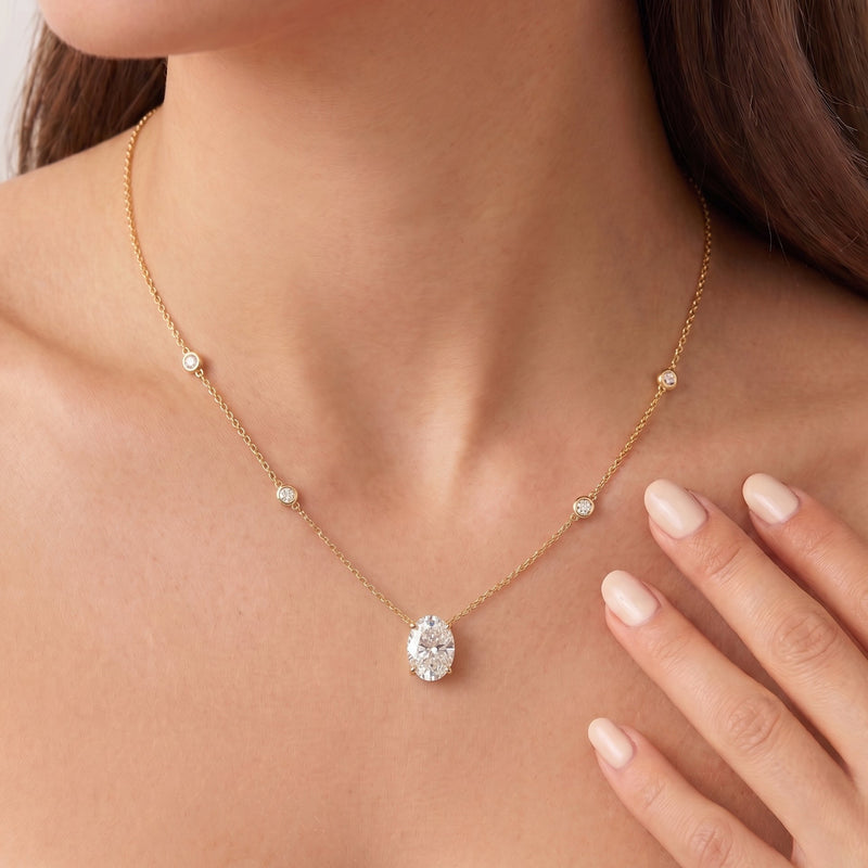 A  close up of a model wearing The Juliette Necklace in yellow gold, featuring a delicate chain with four small round bezel-set lab-grown diamonds spaced along the chain, ending with an oval-cut lab-grown diamond solitaire pendant - The Jewel Concierge