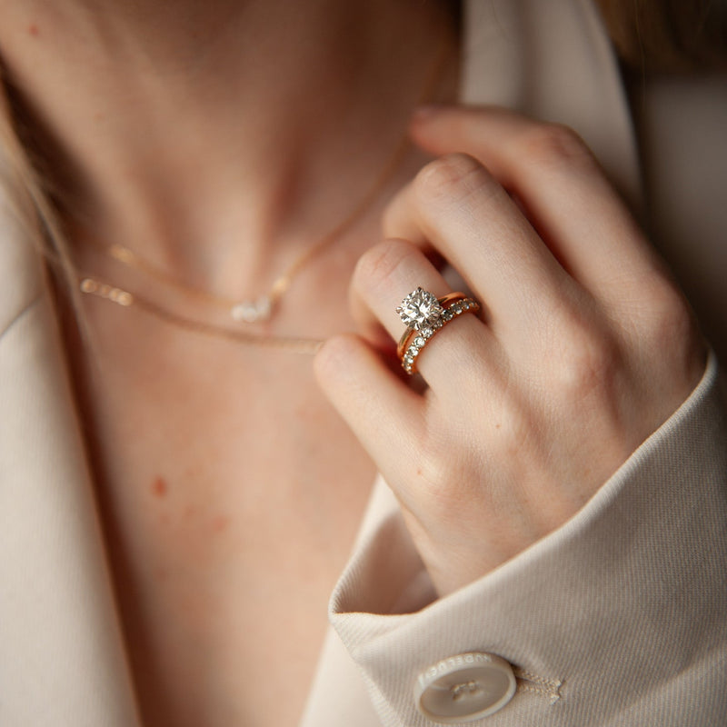 A close-up lifestyle shot of a round cut lab-grown diamond engagement in 18k rose gold, styled with a pave wedding ring  | The Jewel Concierge