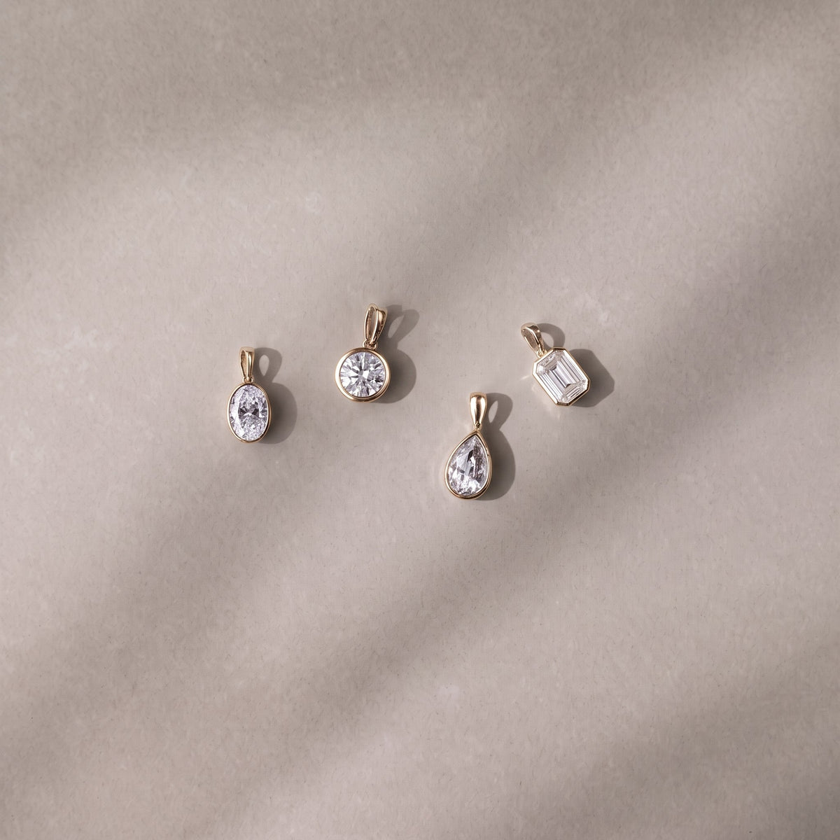 Four Odette Bezel pendants in yellow gold, elegantly laid on a luxurious grey background - The Jewel Concierge