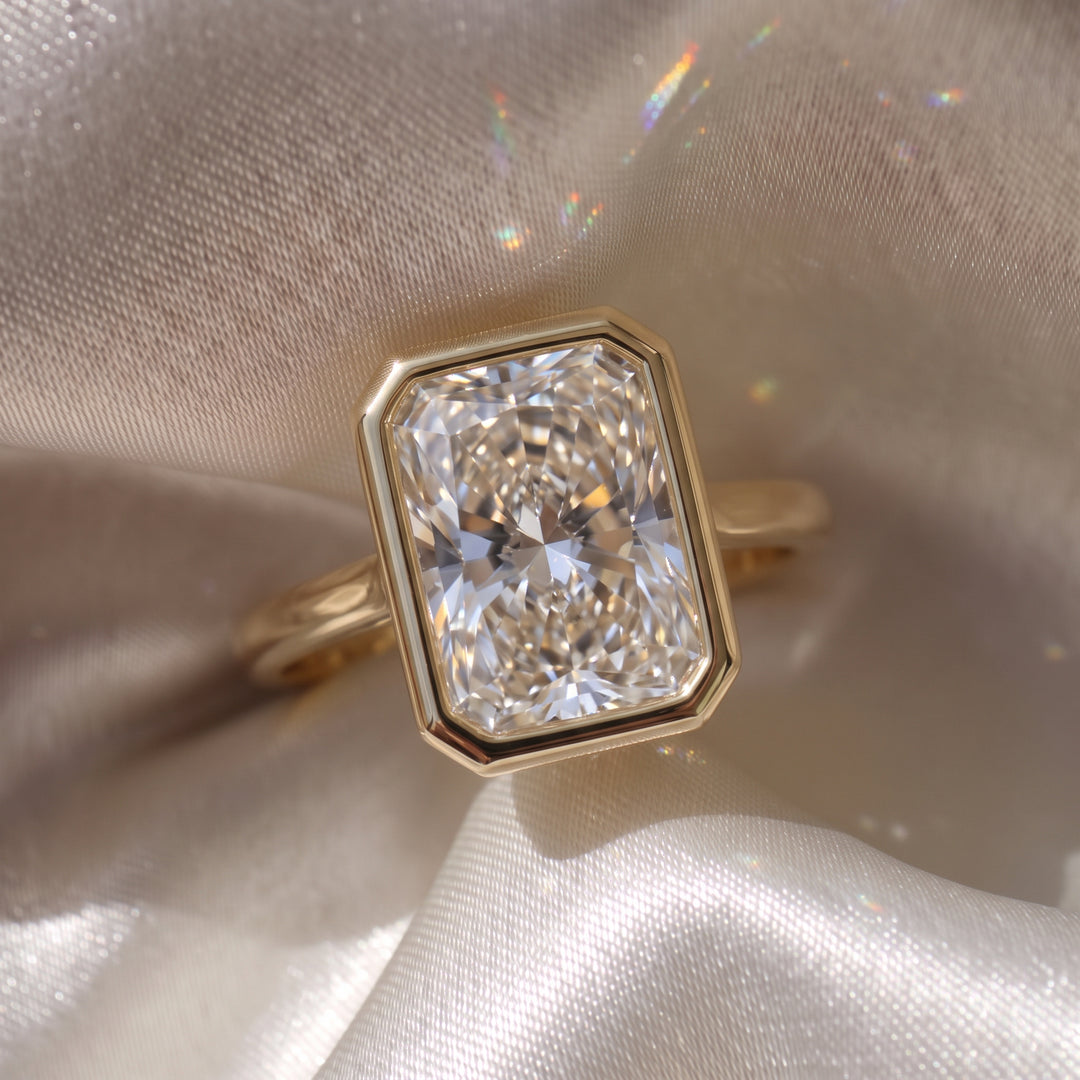 The Polaris Ring - Radiant Bezel Solitaire in 18K yellow gold, laid elegantly on a silk fabric - The Jewel Concierge