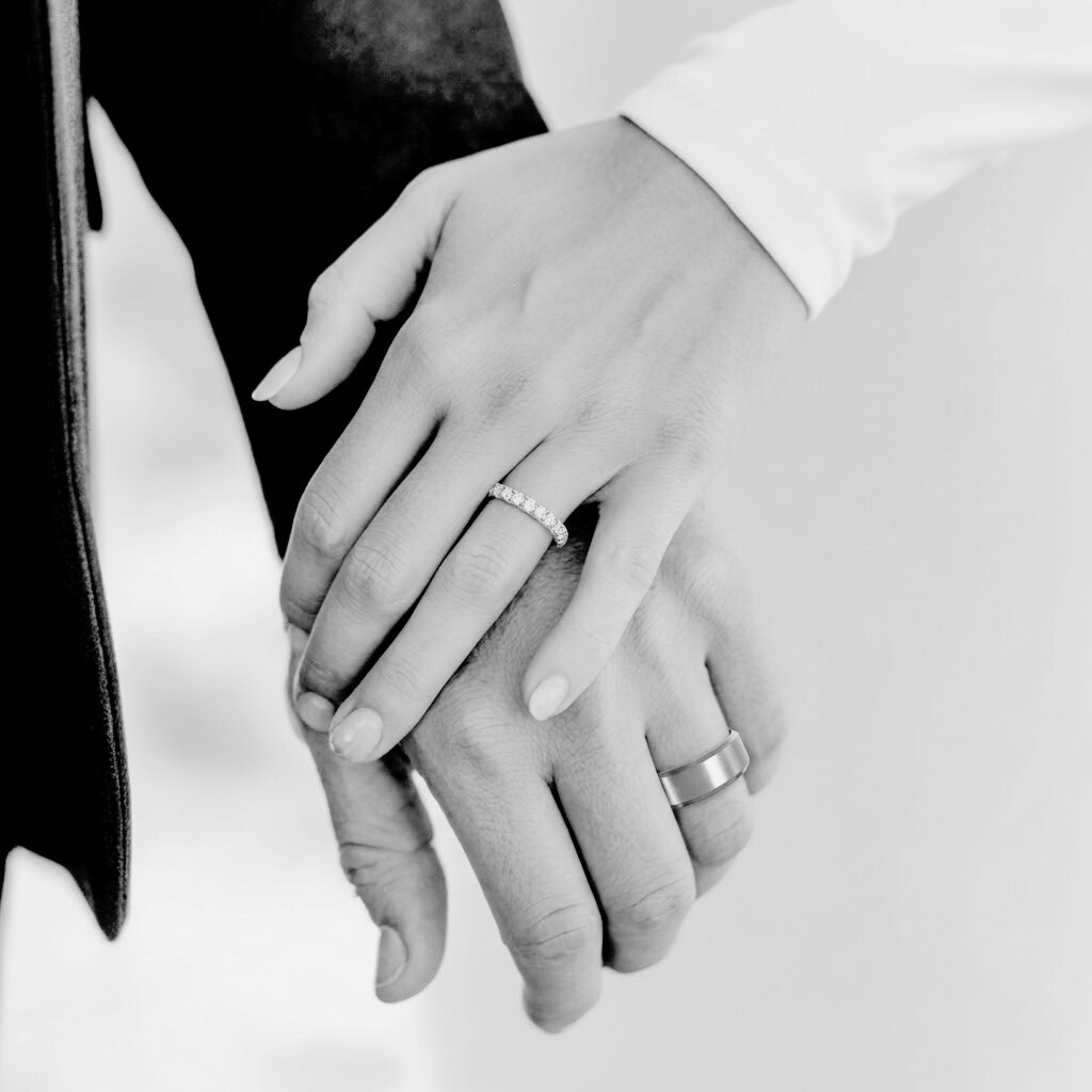 Black and white photo of a bride & groom wearing their wedding rings while holding hands | The Jewel Concierge