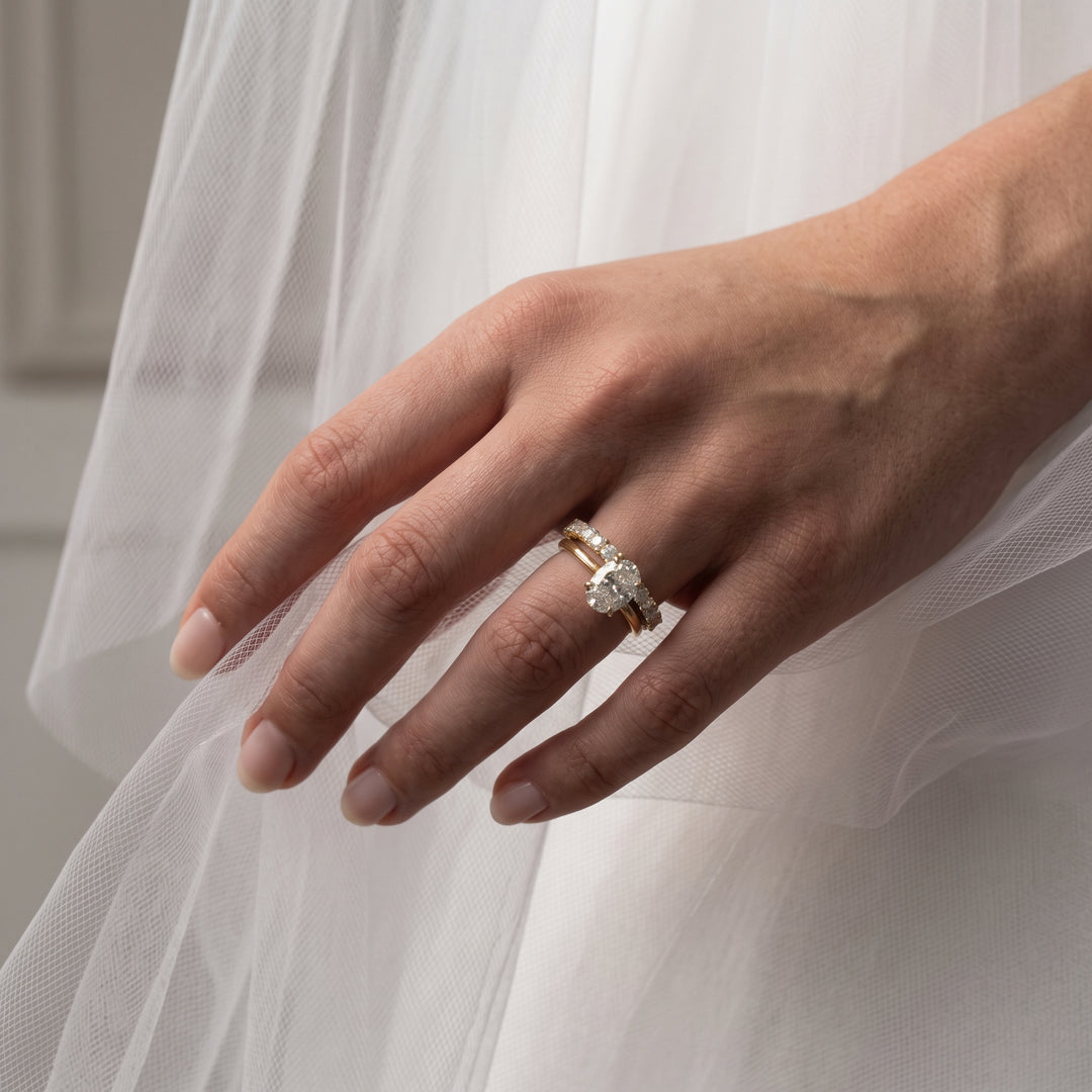 Close up of a bride on her wedding day, showcasing a ring stack featuring a yellow gold oval cut engagement ring and matching pave wedding band with round cut diamonds - The Jewel Concierge