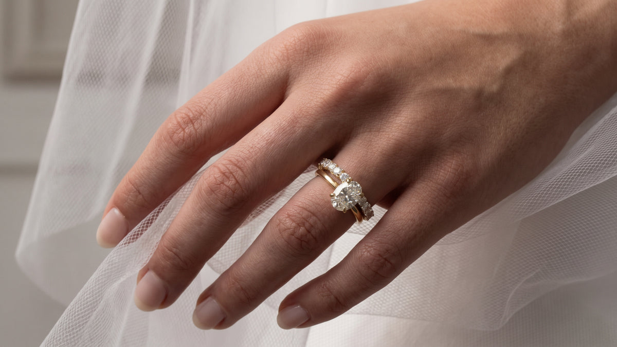 Close up of a bride on her wedding day, showcasing a ring stack featuring The Nova Oval Solitaire along with The Olivia pave wedding band - The Jewel Concierge