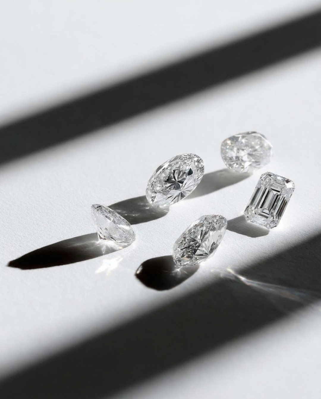 Five lab grown diamonds of different shapes and sizes on a light gray background | The Jewel Concierge