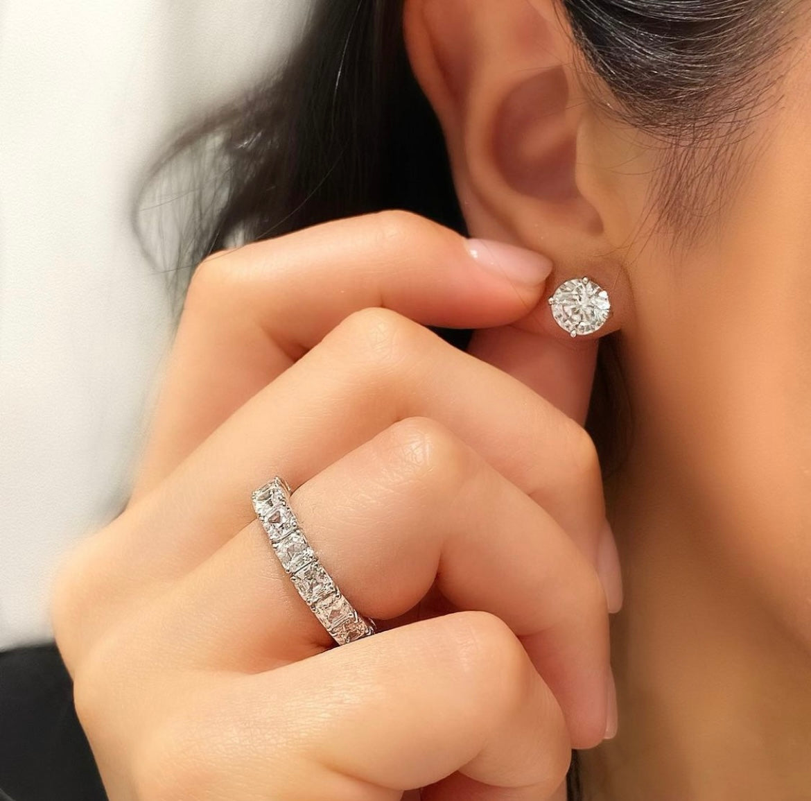 Close-up of a woman wearing diamond earrings and an eternity diamond ring.