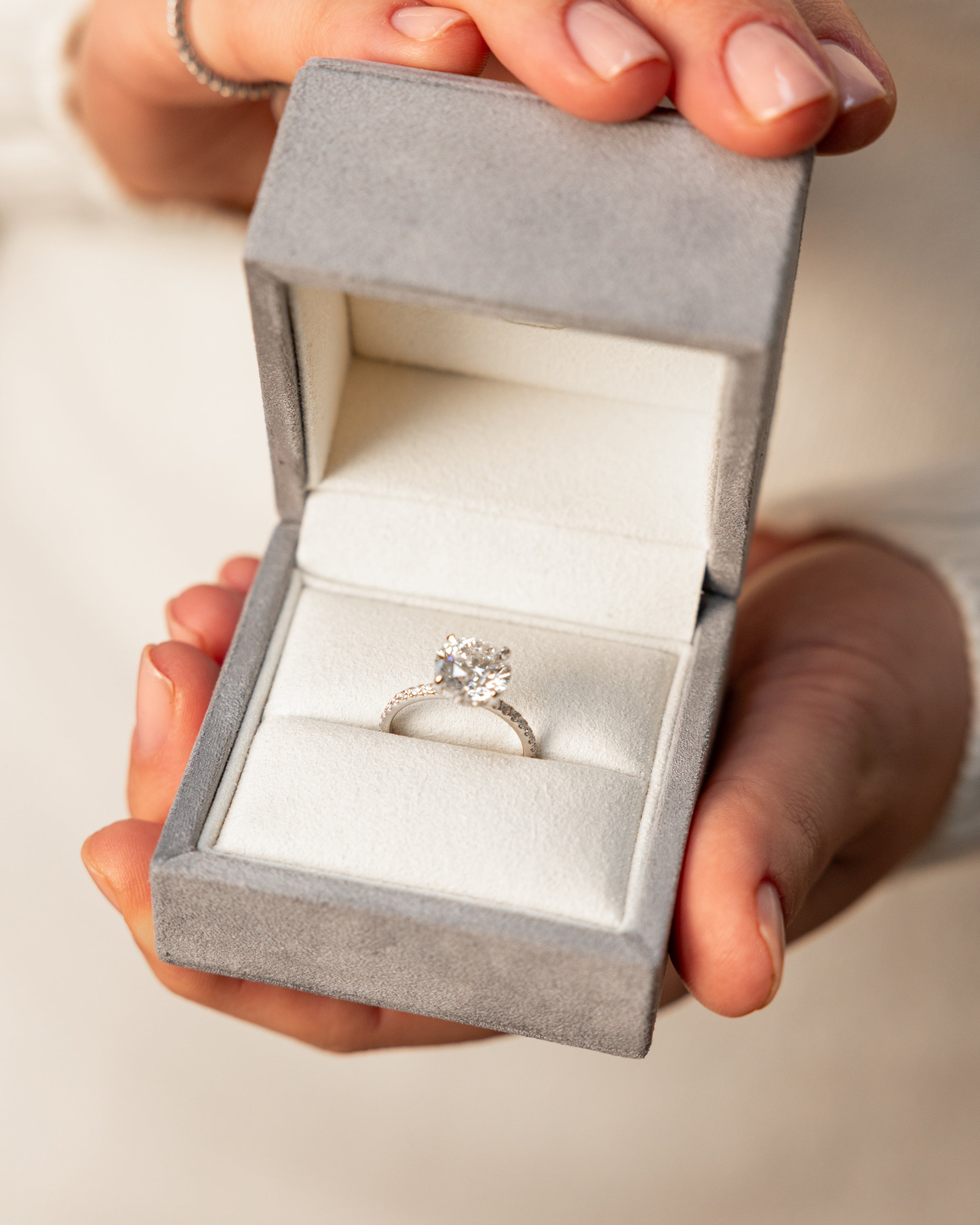 woman shoecasing a dazzling lab-grown diamond engagement ring in The Jewel Concierge signature gray velvet ring box 