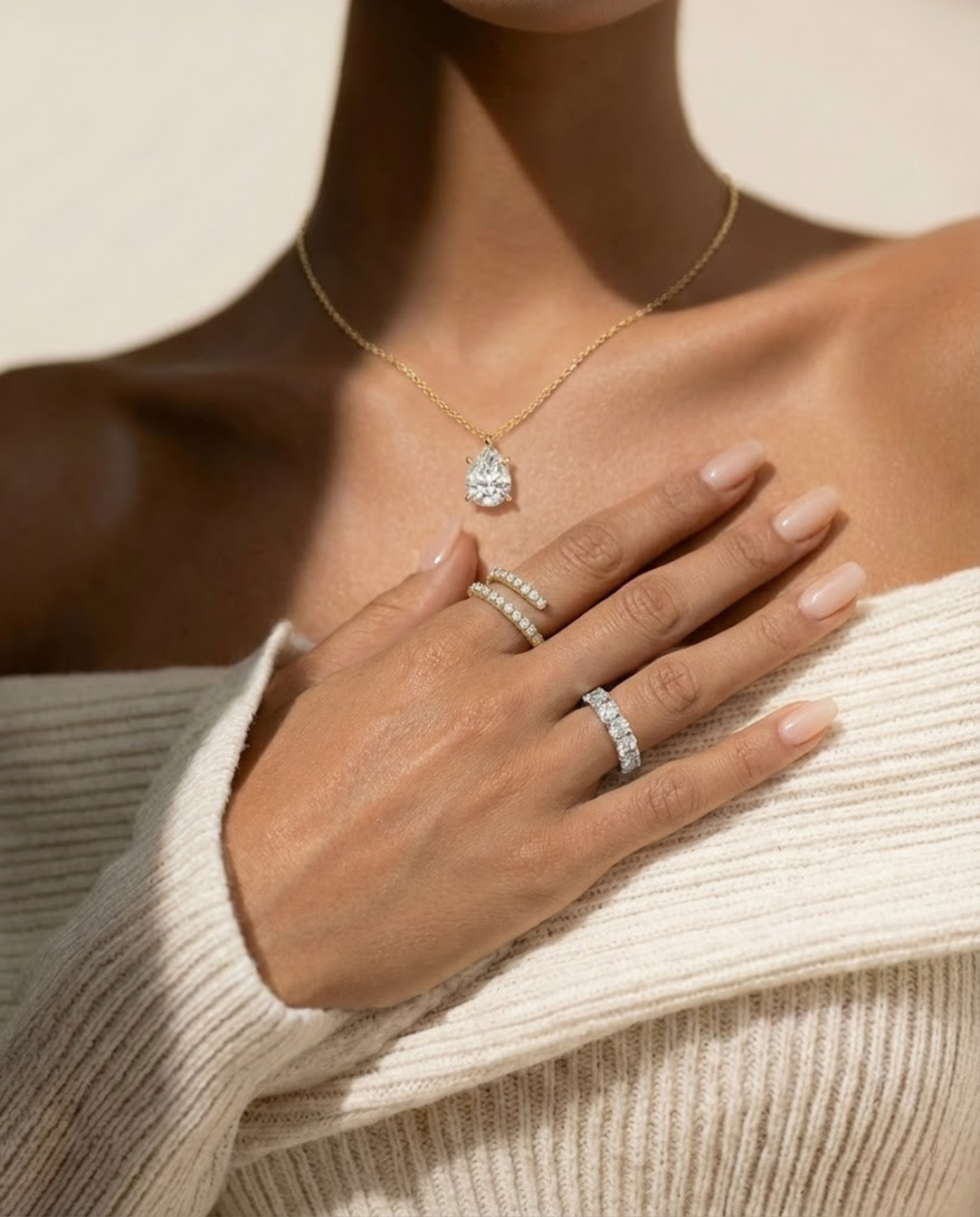 Close-up of a woman's hand wearing multiple diamond rings with a pear cut diamond necklace.