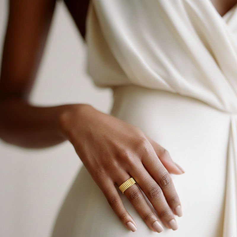 Close-up of a hand wearing a gold ring on a neutral background